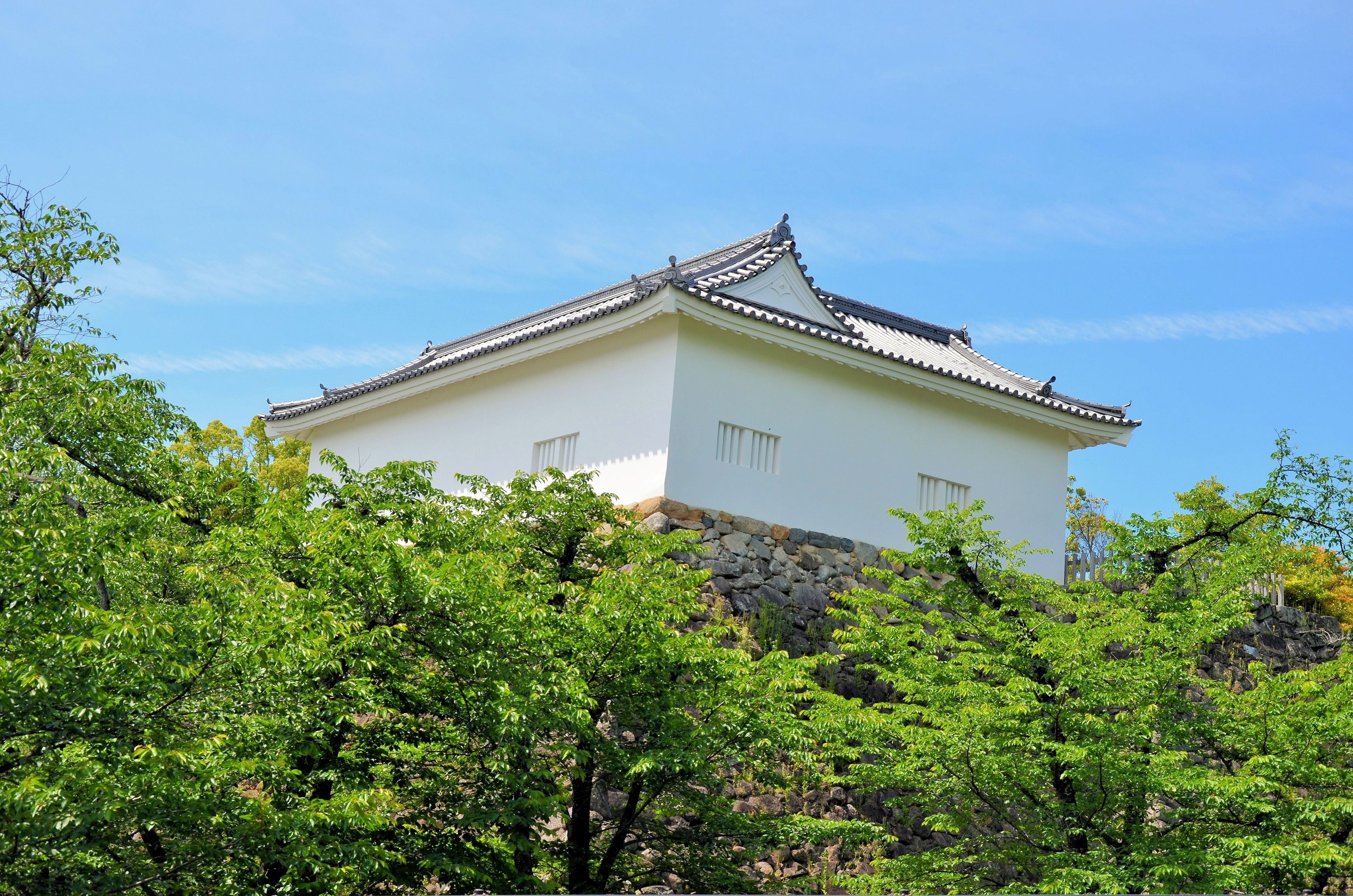 A traditional Japanese building with a tiled roof, surrounded by lush green trees.