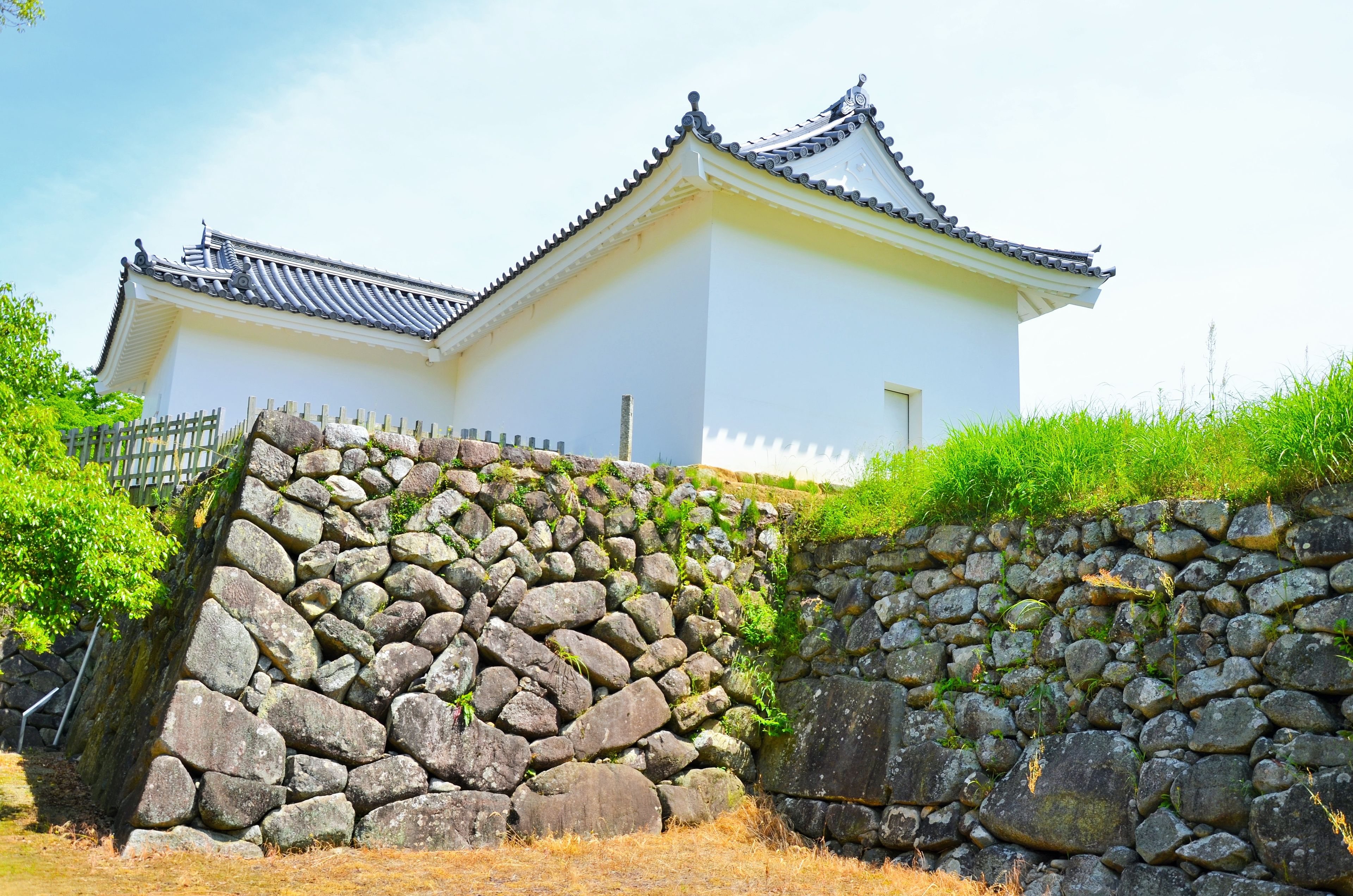 A traditional Japanese castle with white walls and tiled roofs, surrounded by stone walls and greenery.