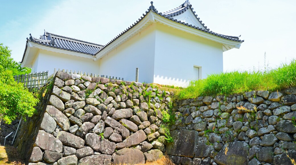 A traditional Japanese castle with white walls and tiled roofs, surrounded by stone walls and greenery.