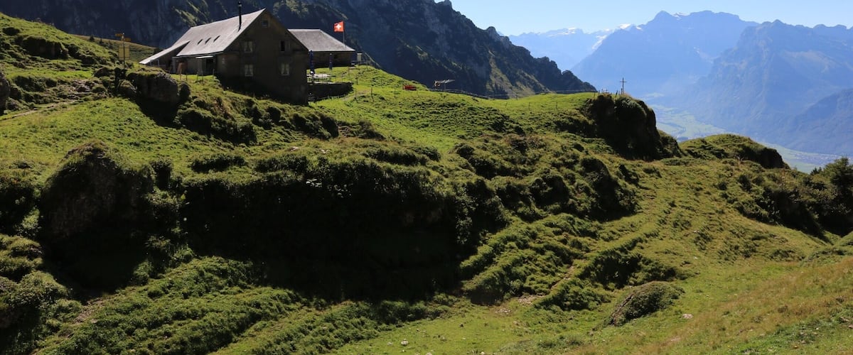 A house on a grassy hillside with mountains in the background.