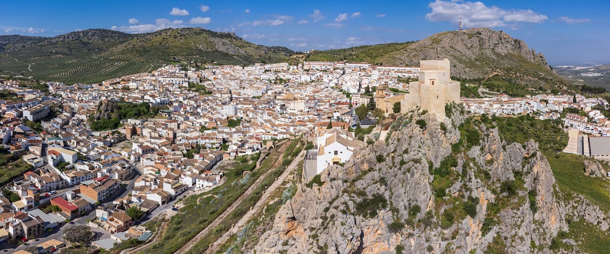 A coastal town with a prominent tower on a hill, surrounded by white buildings and green hills.