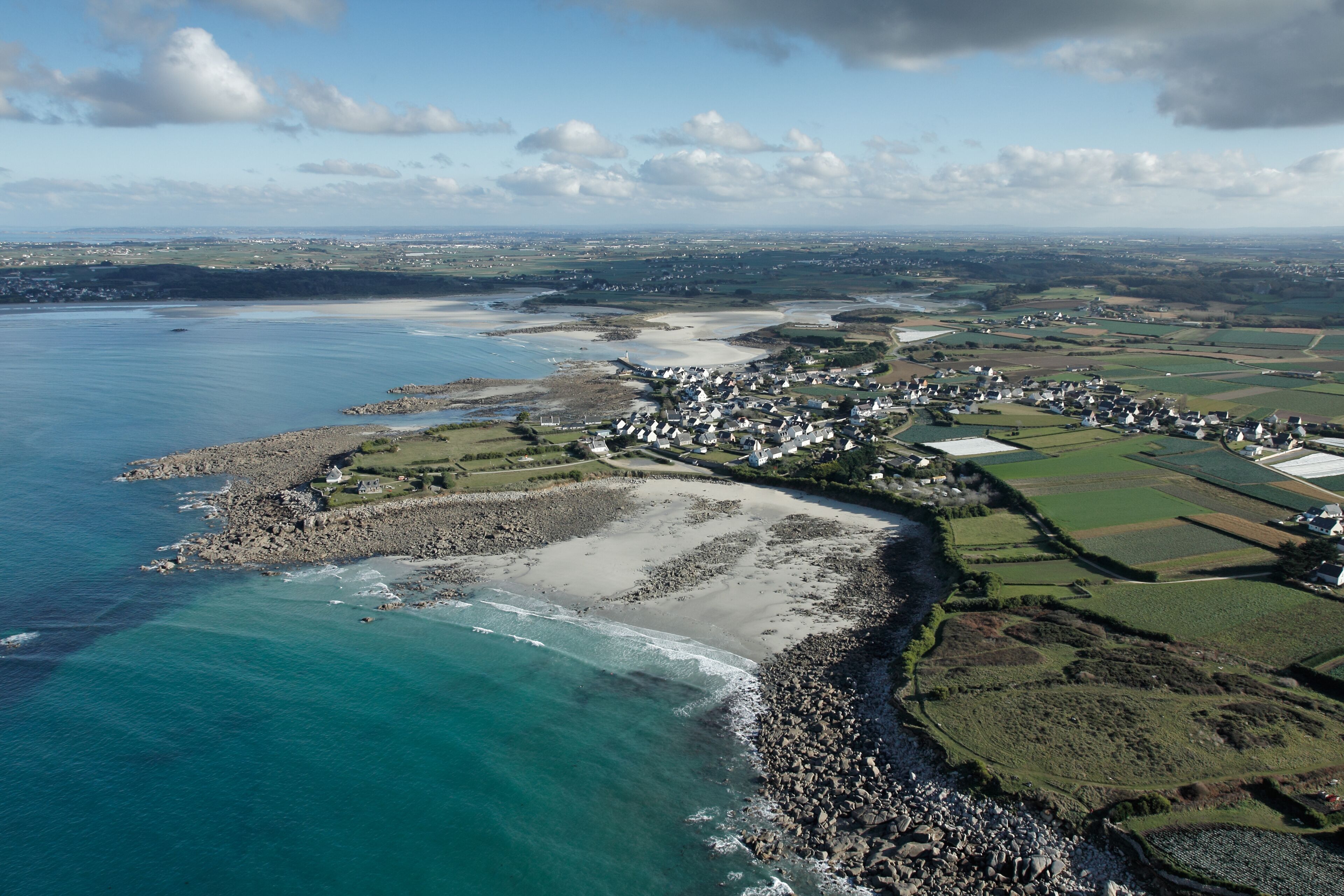 An aerial view of a coastal town with a beach, rocky shoreline, and surrounding fields.