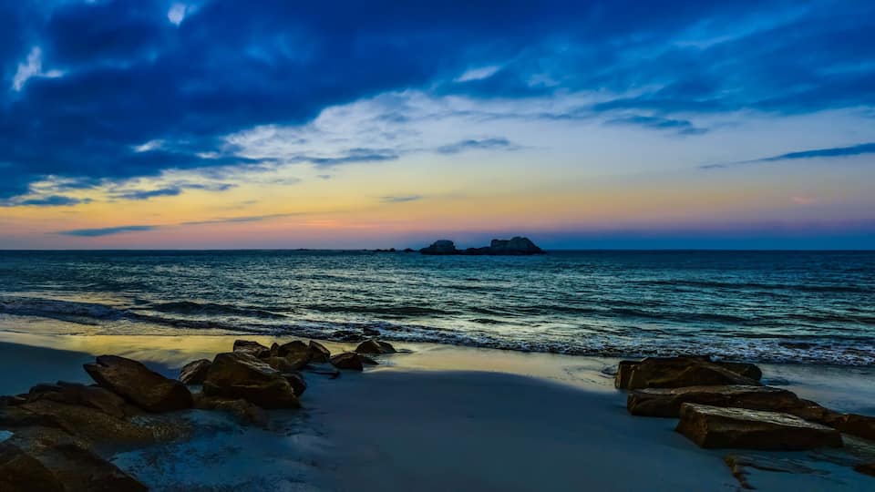 A beach with rocks in the foreground and a sunset over the ocean.