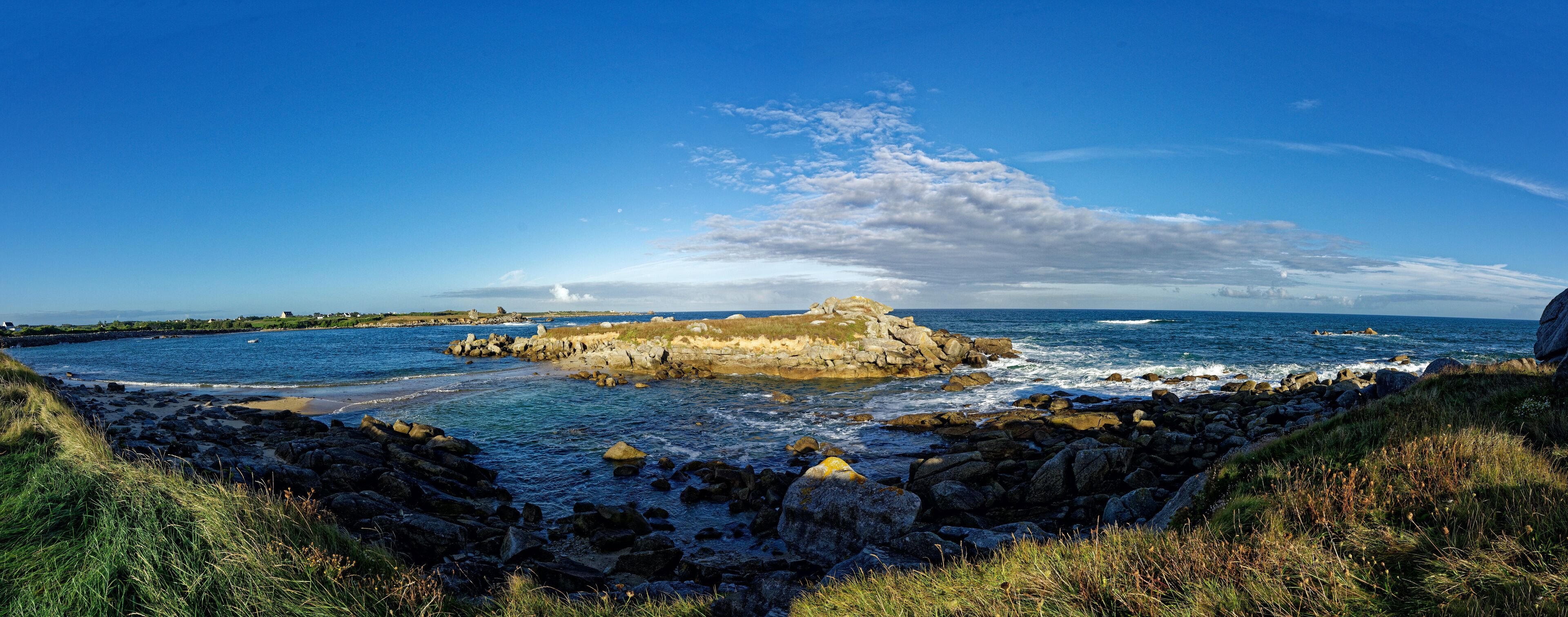 A rocky coastline with a prominent rock formation in the center, surrounded by ocean waves and a clear blue sky.