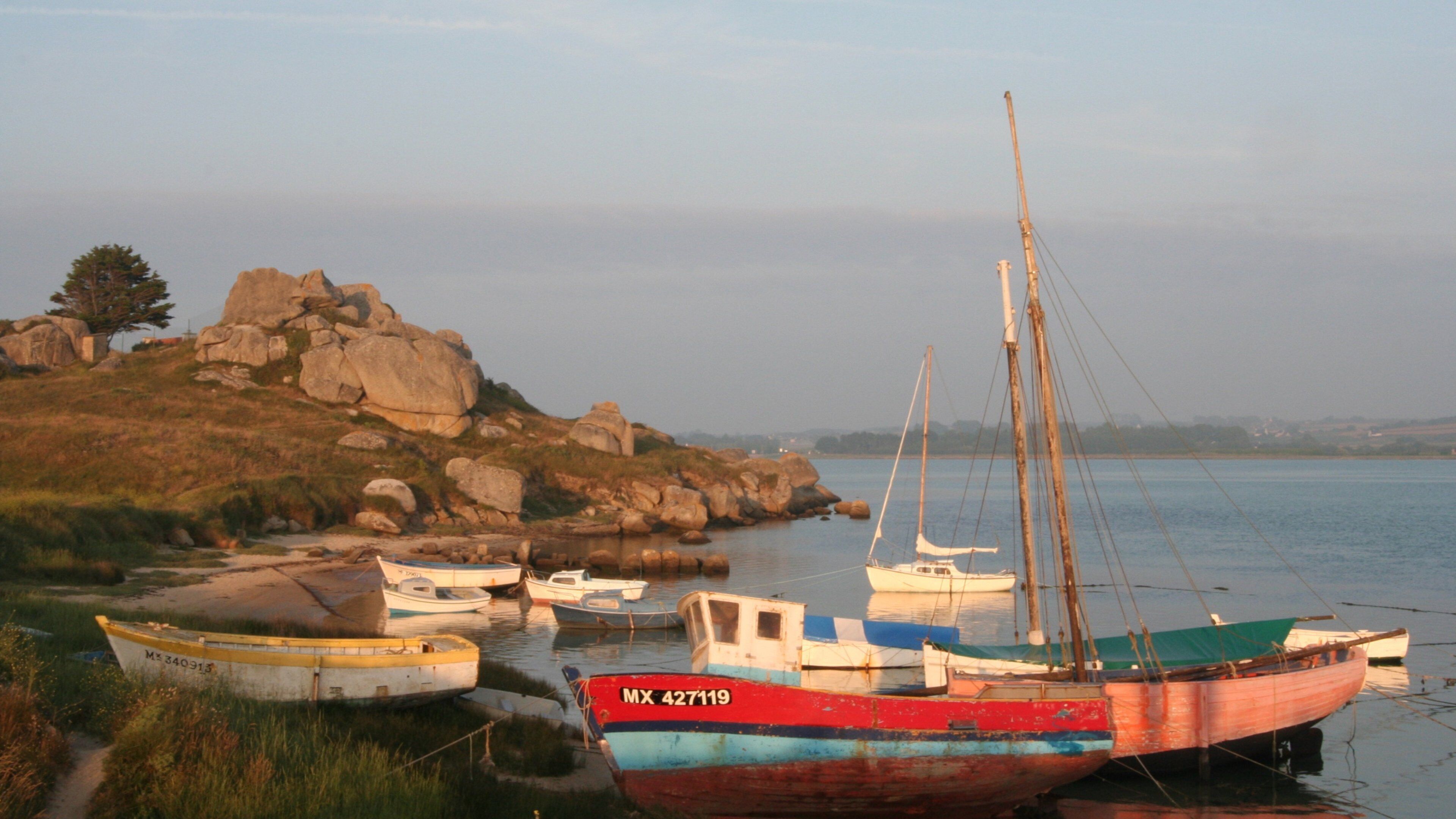 A rocky shoreline with several boats moored near the water's edge.