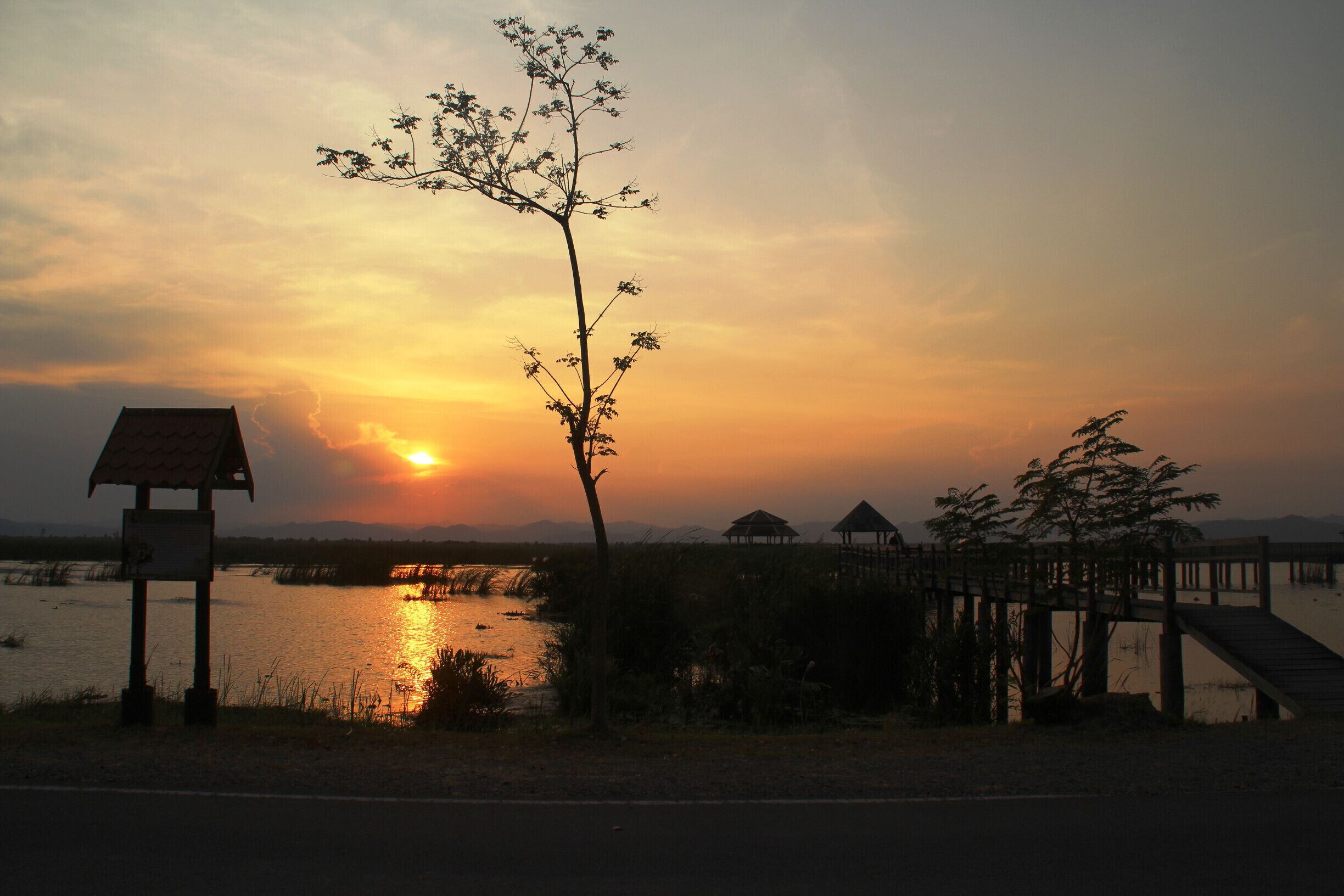Um pôr do sol sobre um lago, com um píer de madeira e um coreto.