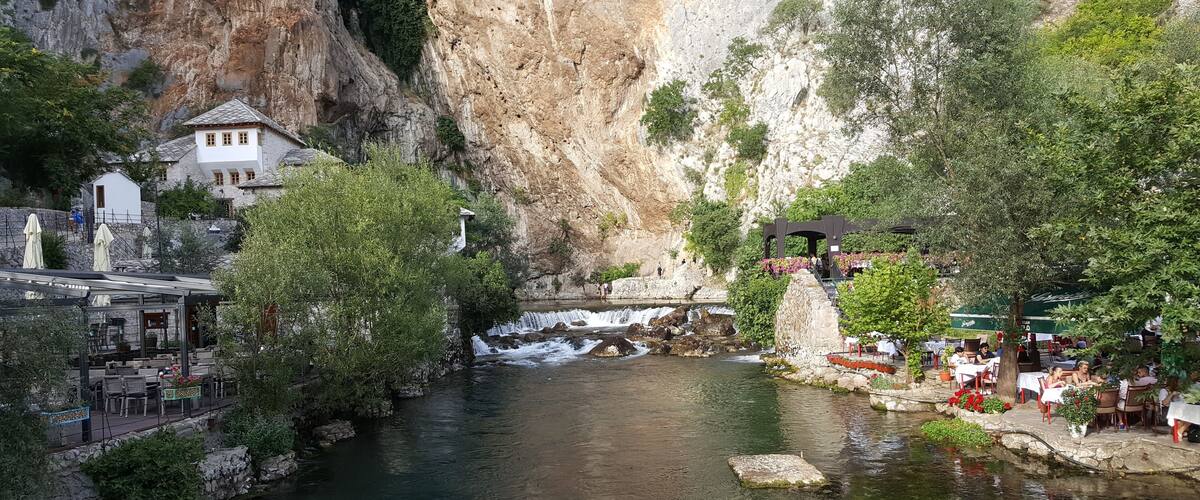 A river flowing through a canyon with a waterfall, surrounded by lush greenery and a restaurant area.