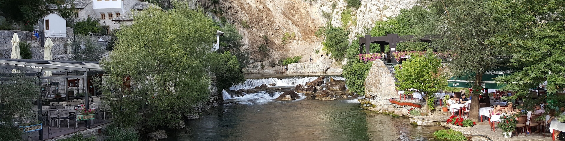 A river flowing through a canyon with a waterfall, surrounded by lush greenery and a restaurant area.