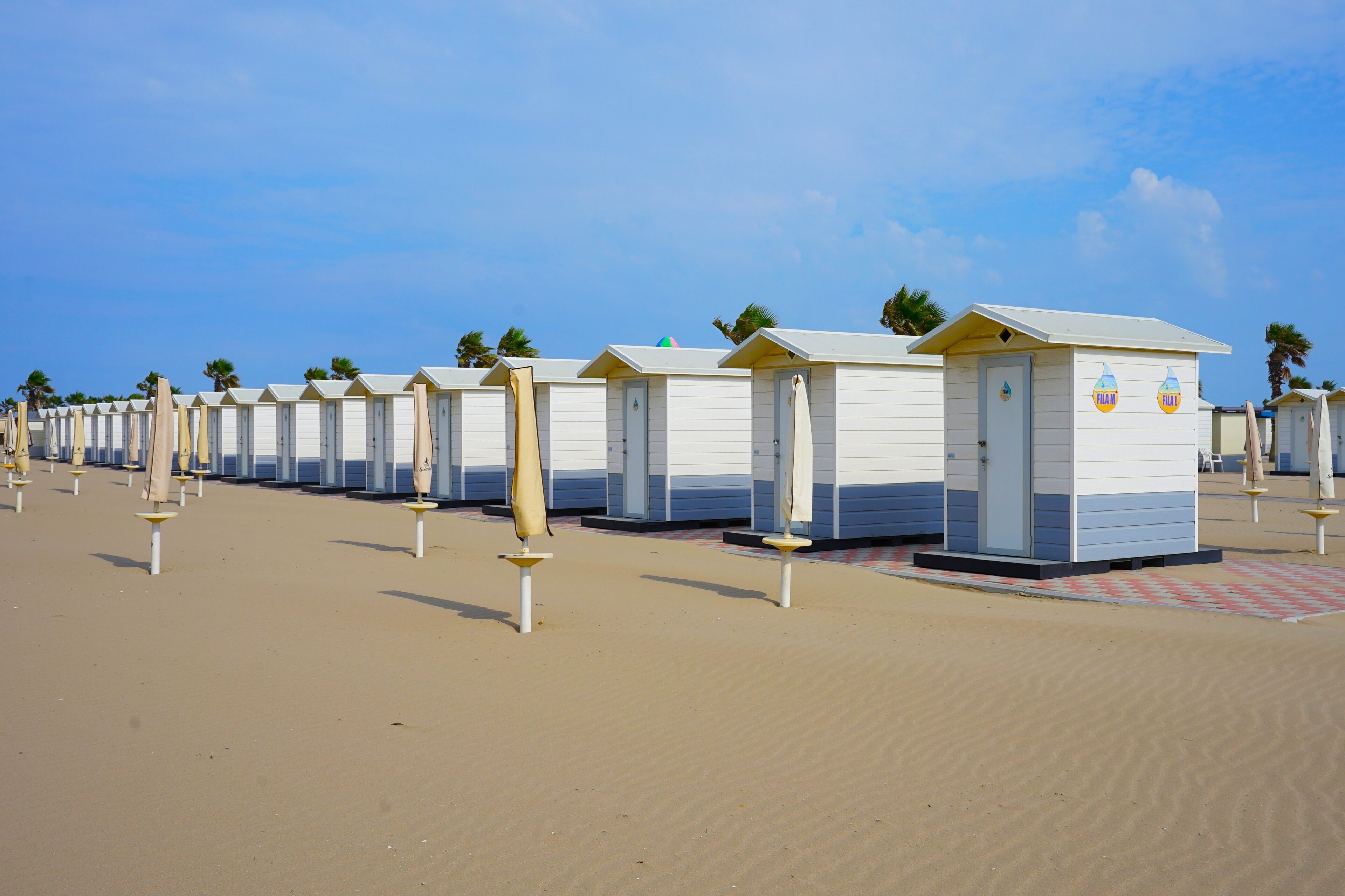A row of beach huts with umbrellas on a sandy beach.
