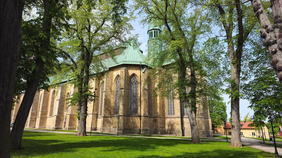 A historic church with a green roof and tall, narrow windows, surrounded by lush green trees.