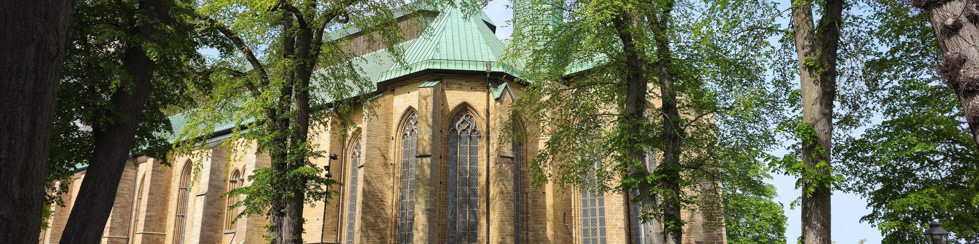 A historic church with a green roof and tall, narrow windows, surrounded by lush green trees.