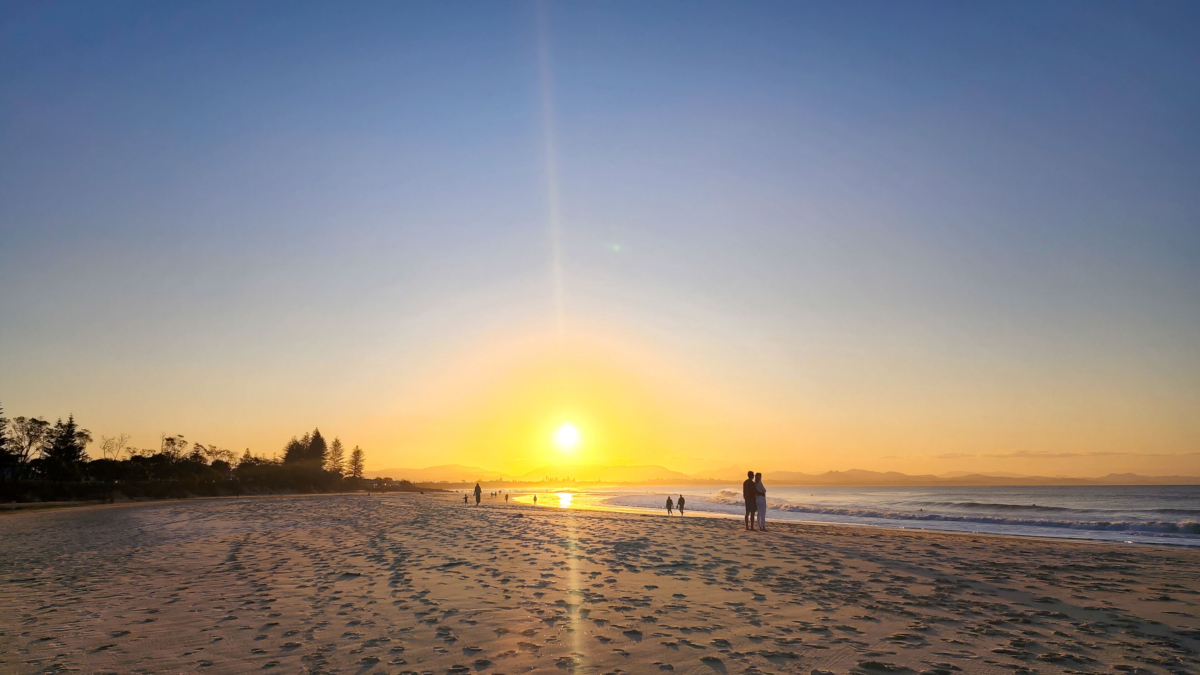 Uma praia ao pôr do sol, com pegadas na areia e céu claro.