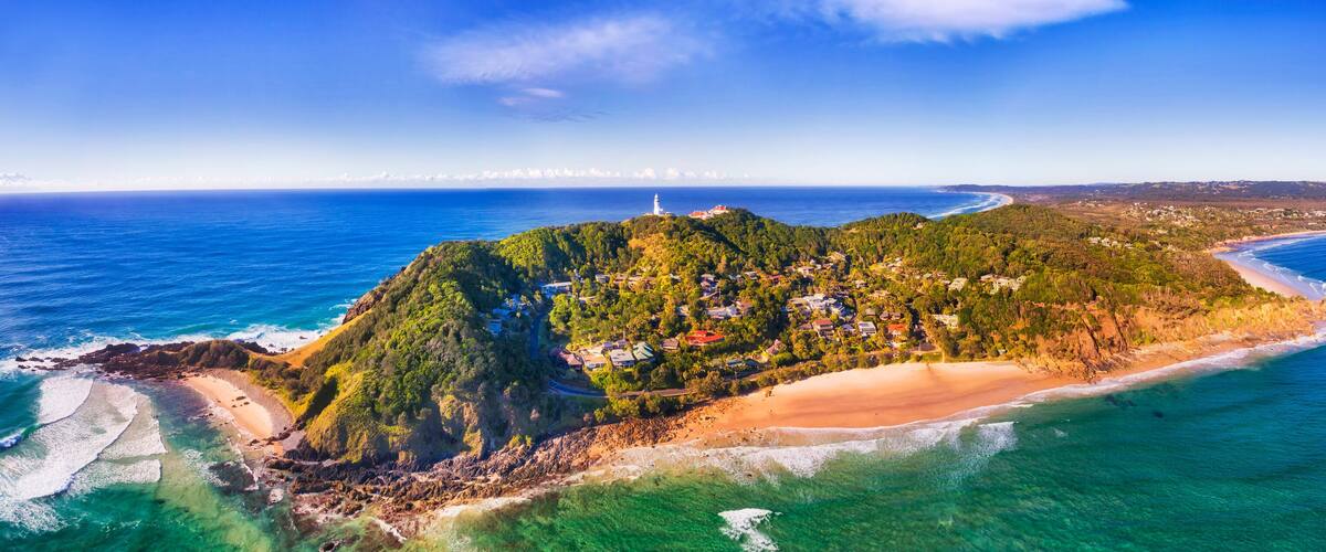 An aerial view of a coastal island with a lighthouse, dense forest, and a sandy beach.