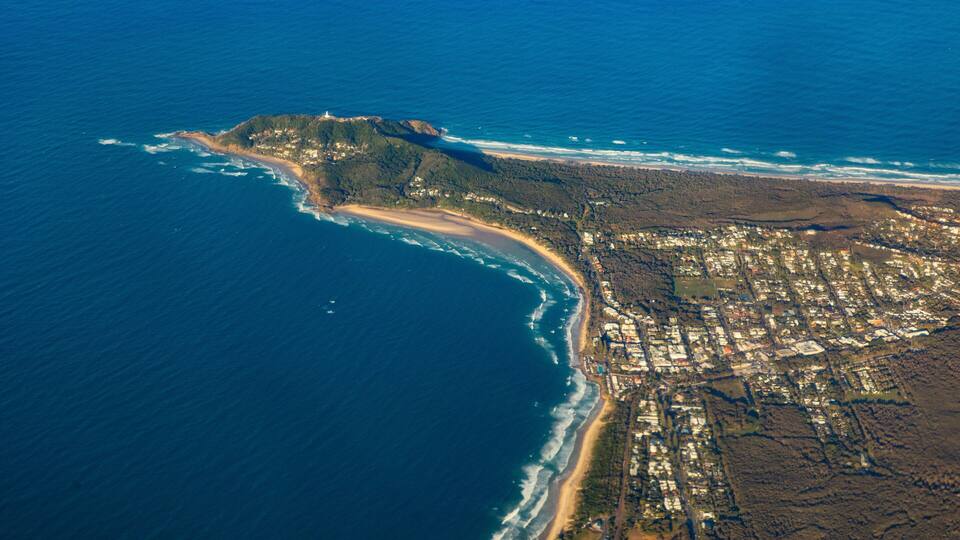 An aerial view of a coastal town with a beach, a lighthouse, and dense residential areas.