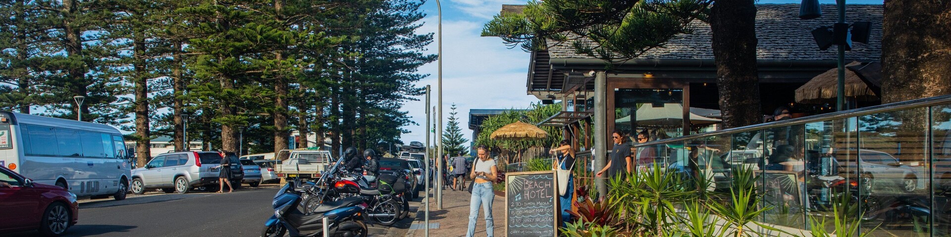 Um café à beira-mar com área externa, motocicletas estacionadas e um ônibus ao fundo.