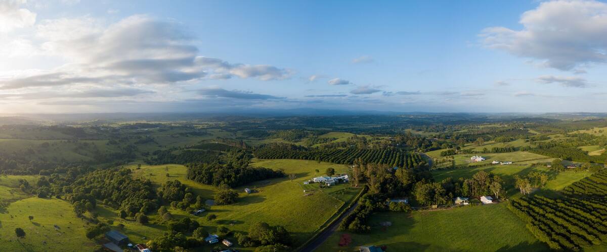 A panoramic view of a lush valley with rolling hills, scattered trees, and a few buildings.