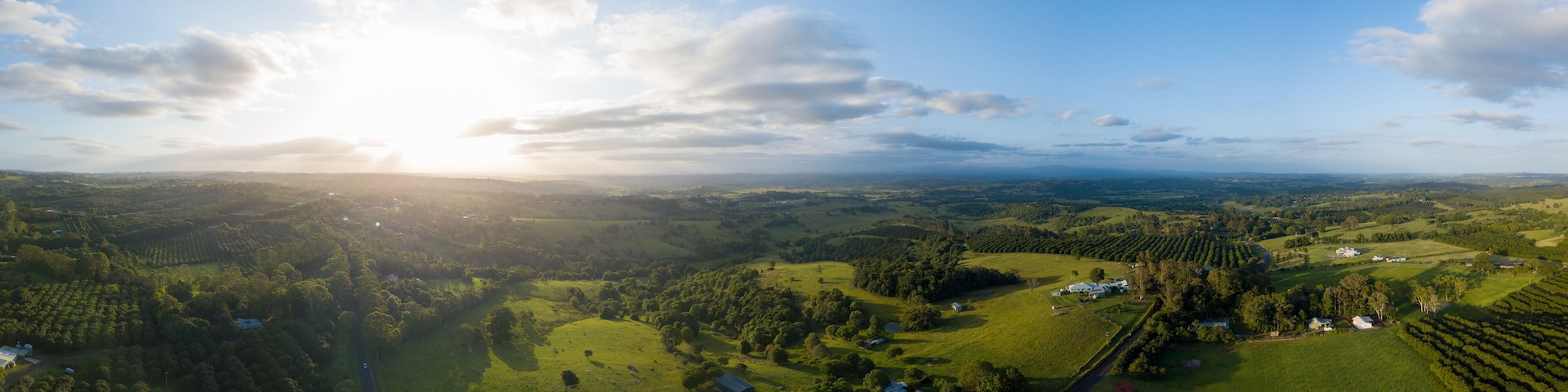 A panoramic view of a lush valley with rolling hills, scattered trees, and a few buildings.