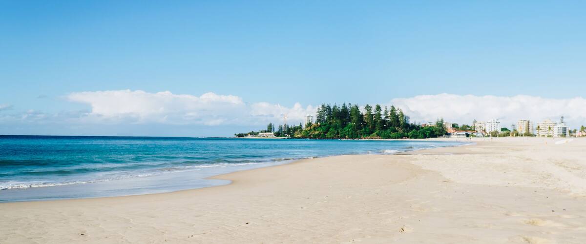 A beach with clear blue water, sandy shore, and a forested island in the background.