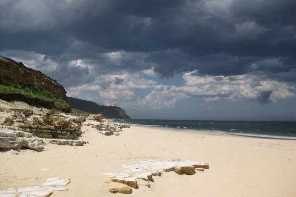 A beach with a rocky shoreline, a sandy path, and a cloudy sky.