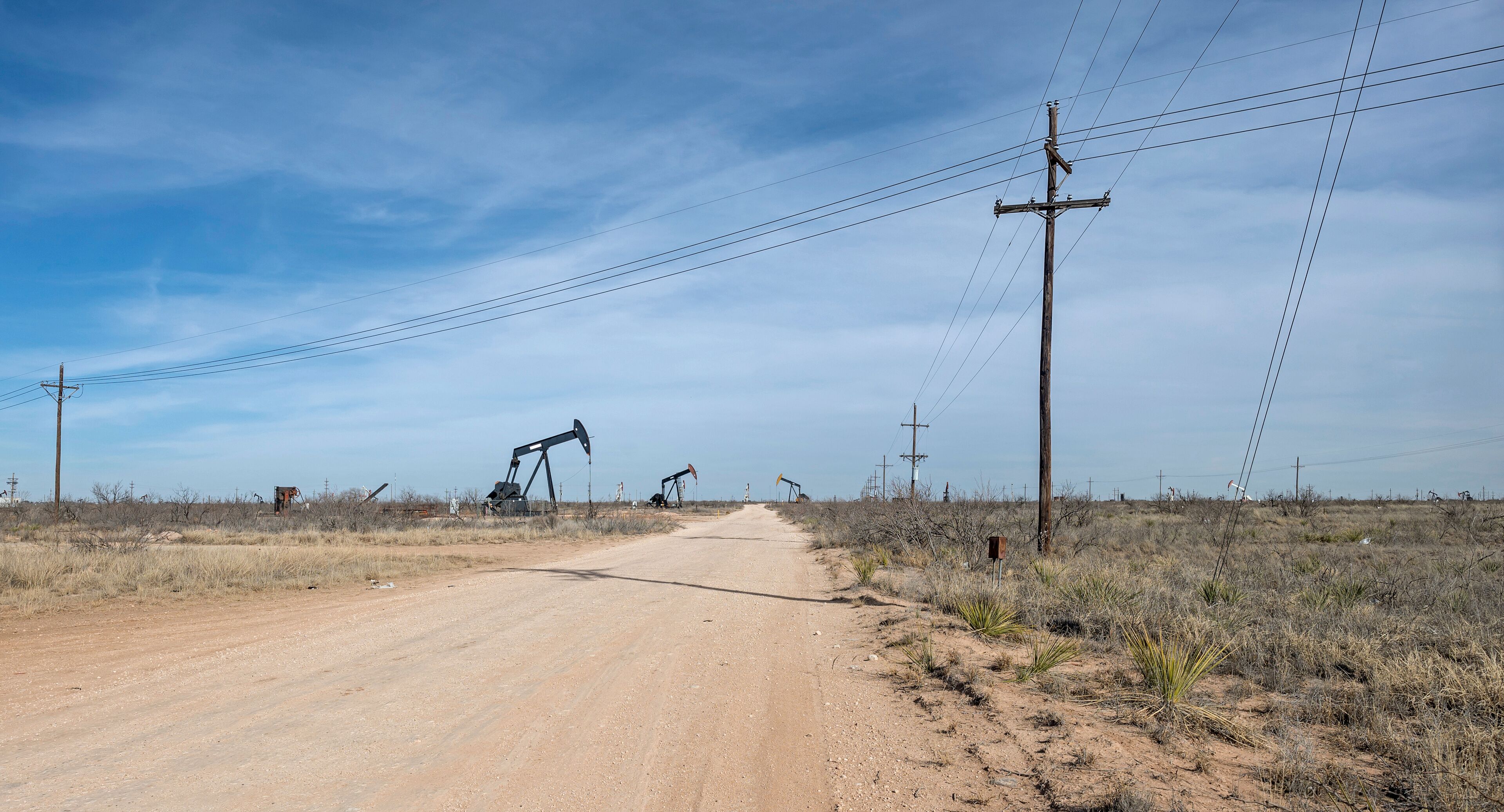 A dirt road with oil pumps in a dry, grassy landscape.