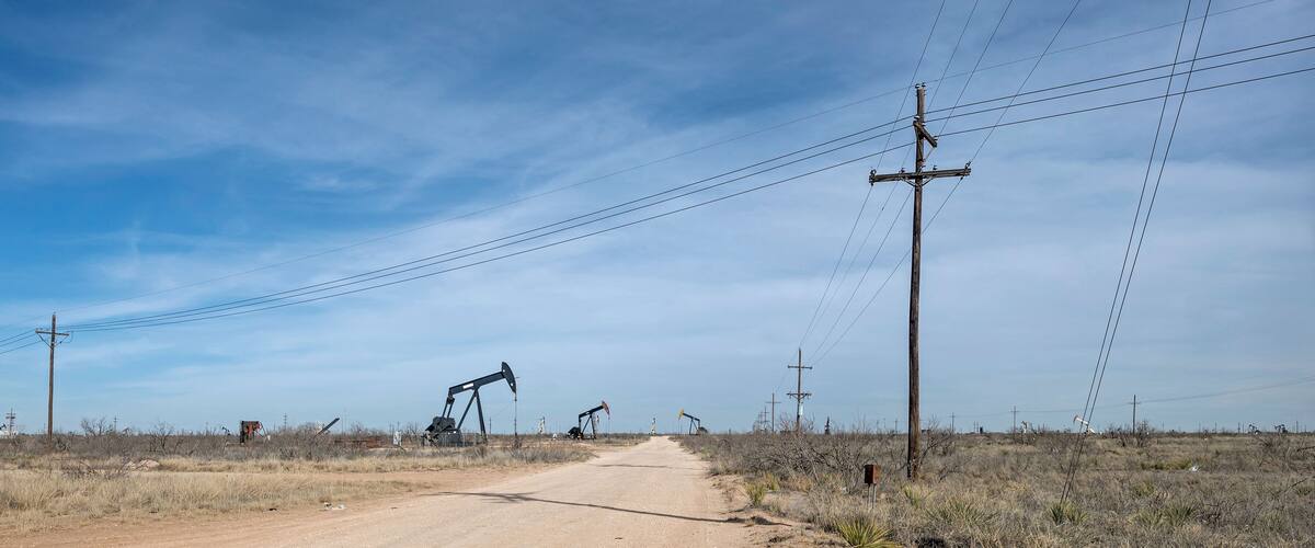 A dirt road with oil pumps in a dry, grassy landscape.