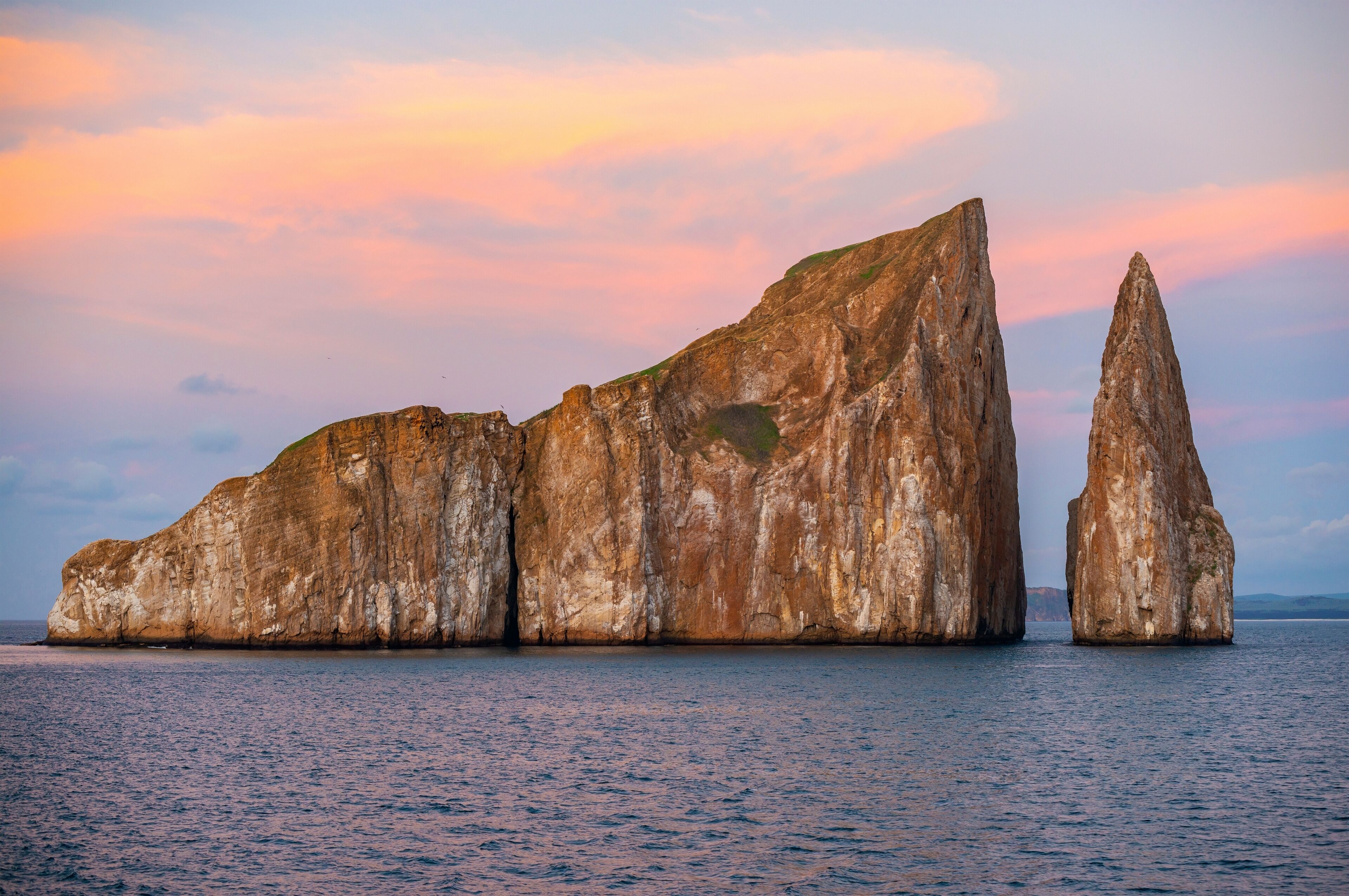 The volcanic rock formation of Kicker Rock (Leon Dormido) at sunset in the Pacific Ocean with sea birds silhouettes flying above the landmark, San Cristobal Island, Galapagos national park, Ecuador.