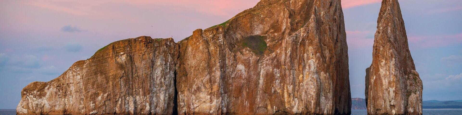 The volcanic rock formation of Kicker Rock (Leon Dormido) at sunset in the Pacific Ocean with sea birds silhouettes flying above the landmark, San Cristobal Island, Galapagos national park, Ecuador.