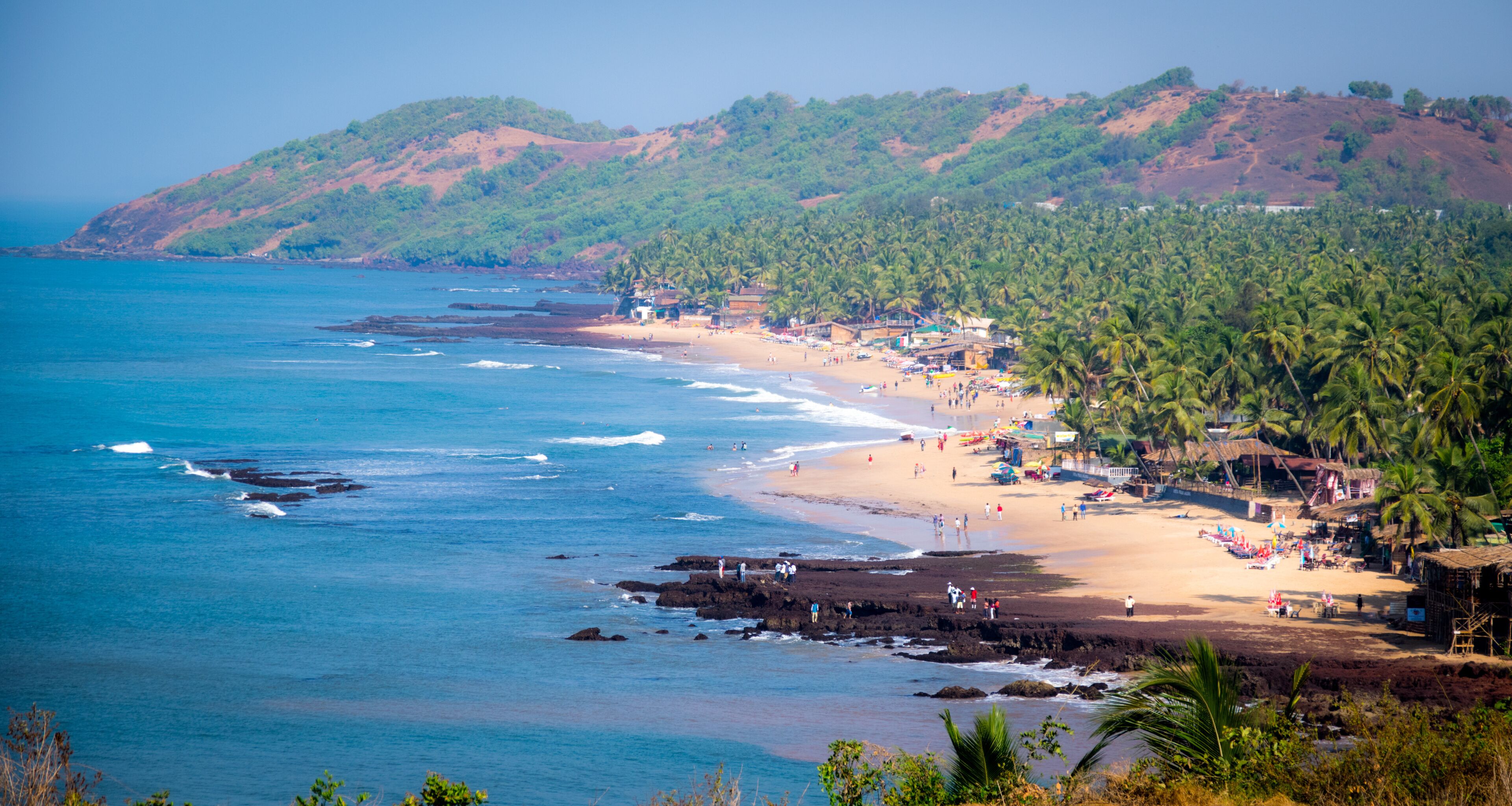 Uma praia com palmeiras, costa rochosa e um relevo montanhoso ao fundo.