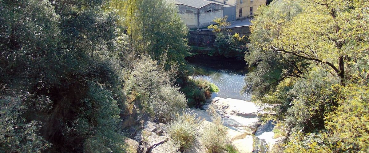 A valley with a river, surrounded by dense forest and a small building complex.