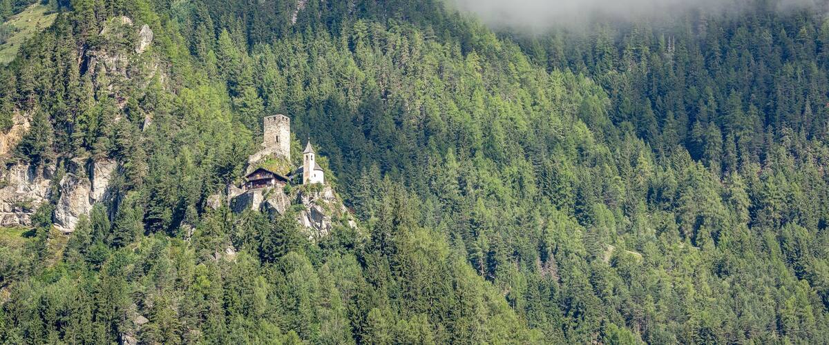 A forested mountain with a historic stone tower and a small building.