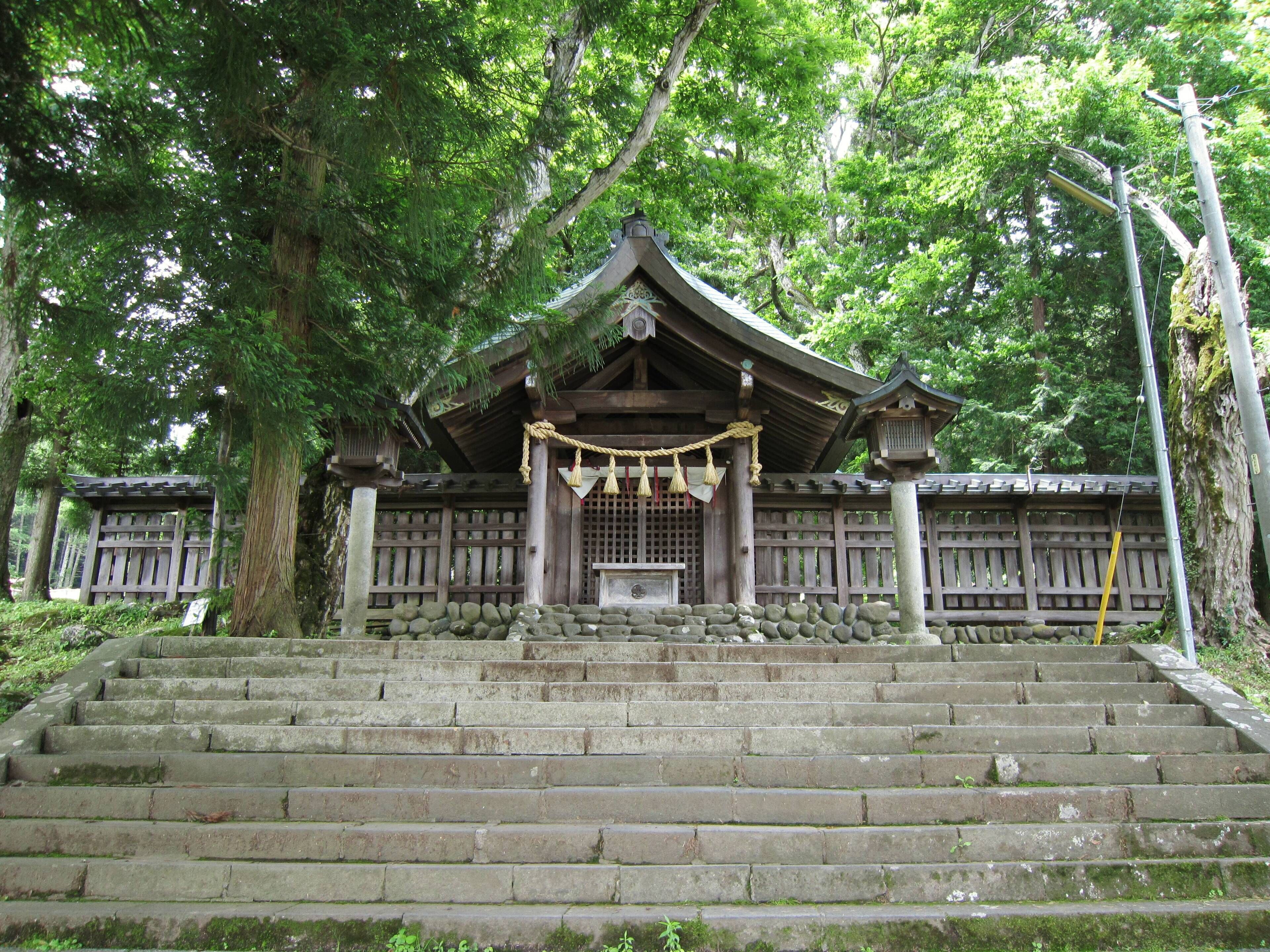 A traditional Japanese temple with stone steps leading up to a wooden structure, surrounded by lush greenery.