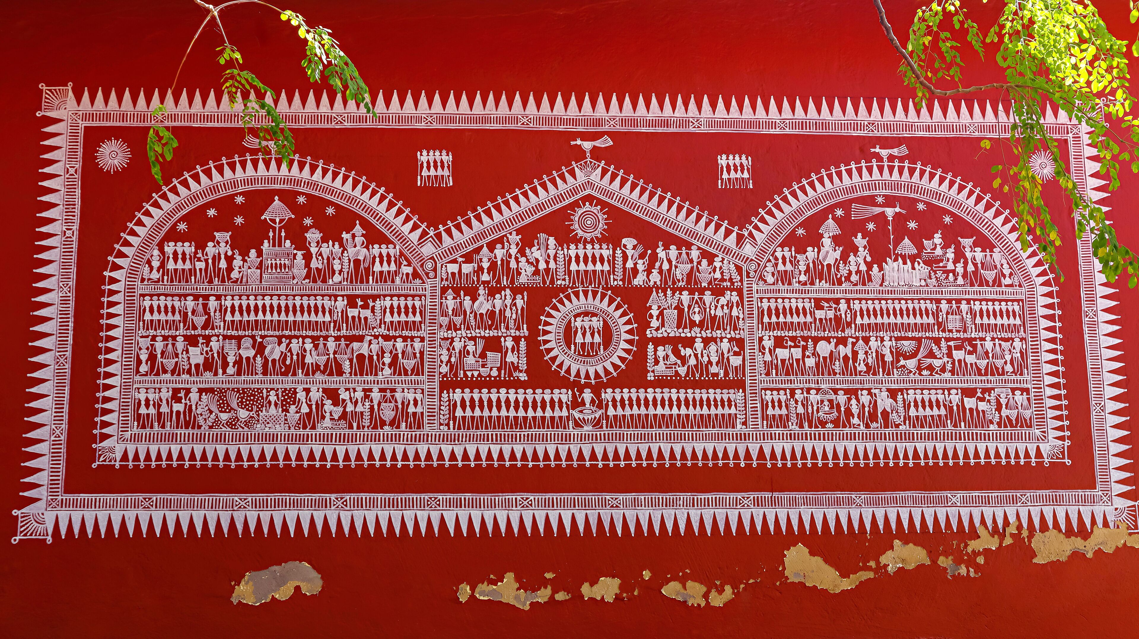 A detailed white painted mural on a red background, depicting various figures and scenes, with some areas of peeling paint.