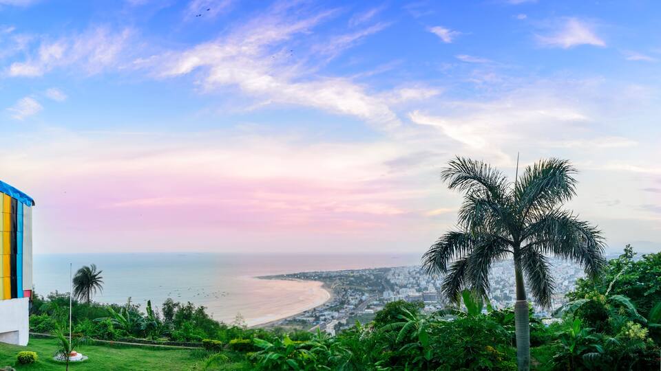 A colorful building overlooking a beach with palm trees and a cityscape in the distance.