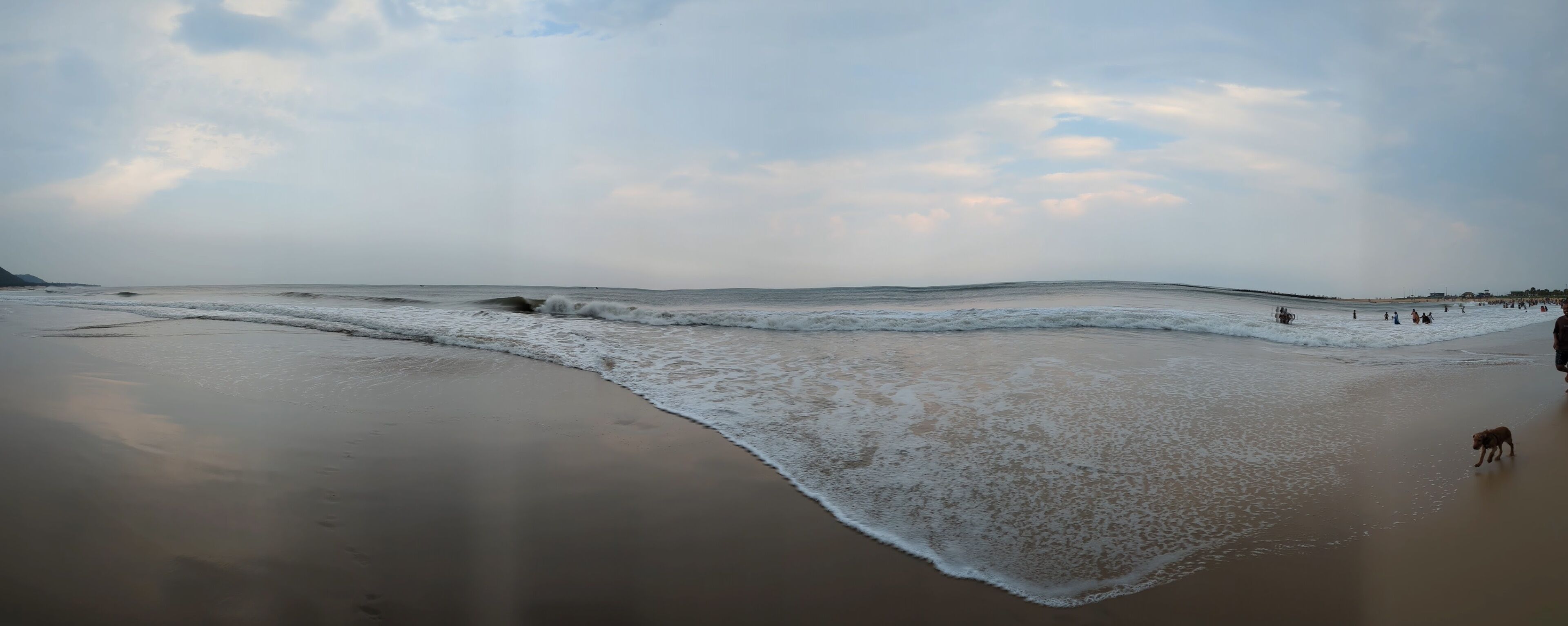 A serene evening at Rushikonda Beach, in Andhra Pradesh, India, with soft golden hues from the setting sun reflecting on the calm, blue waters.