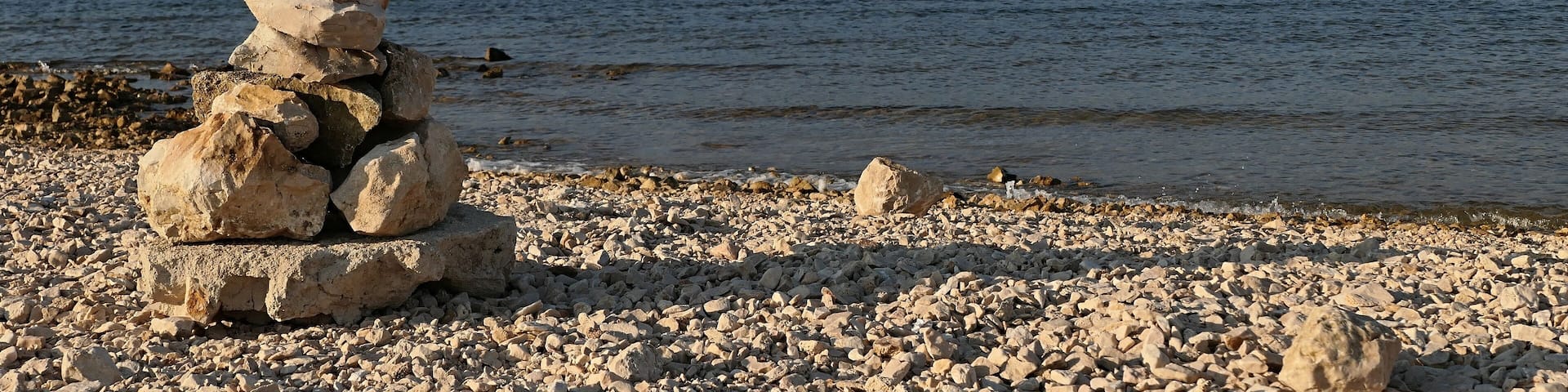 Pile of stones, also called cairn, created on rocky beach north of Razanac, northern Dalmatia, Croatia. Bay water and Velebit mountain visible in background, blue summer skies with some scarce clouds.