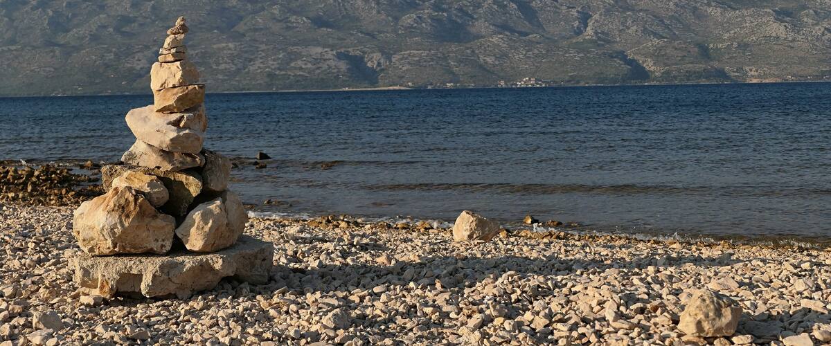 A stack of stones by a rocky shore with a mountain range in the background.