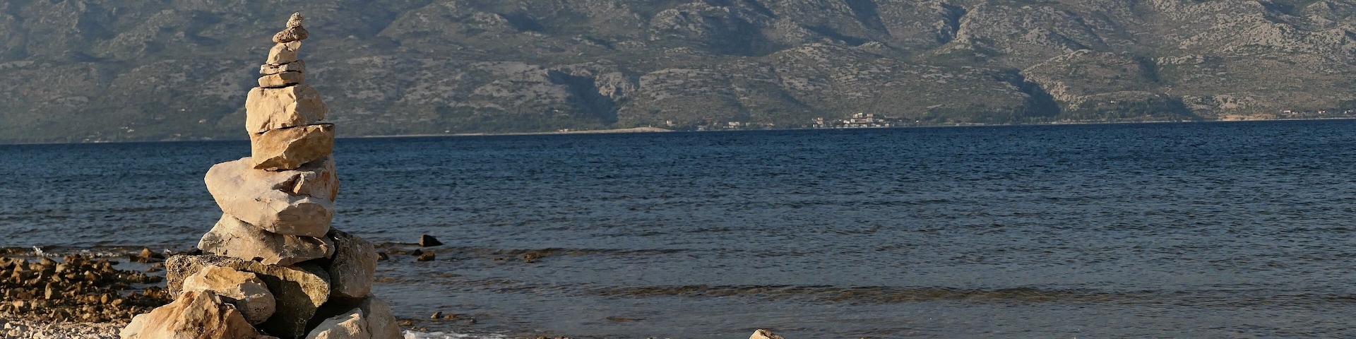 A stack of stones by a rocky shore with a mountain range in the background.