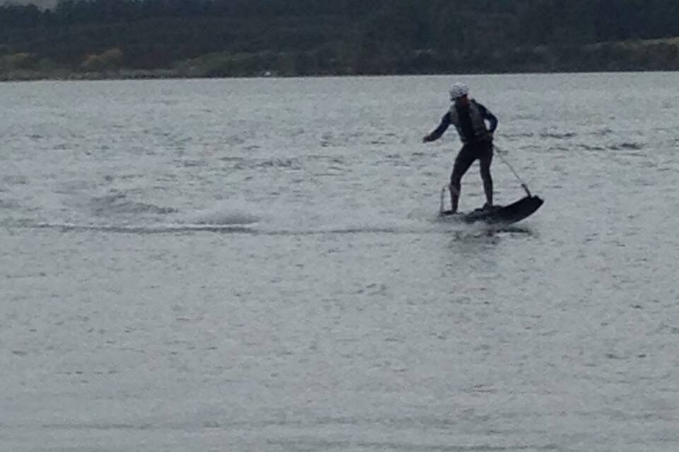 Una persona practicant wakeboard sobre l'aigua, amb muntanyes al fons.