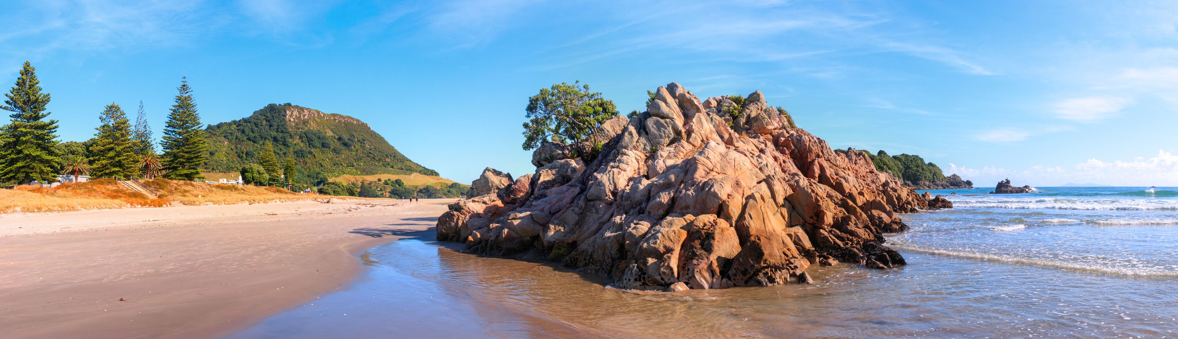 A rocky outcrop on a beach with a mountain in the background.