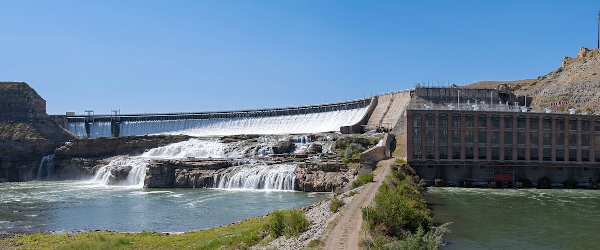 A dam with multiple water spillways and a building adjacent to the river.