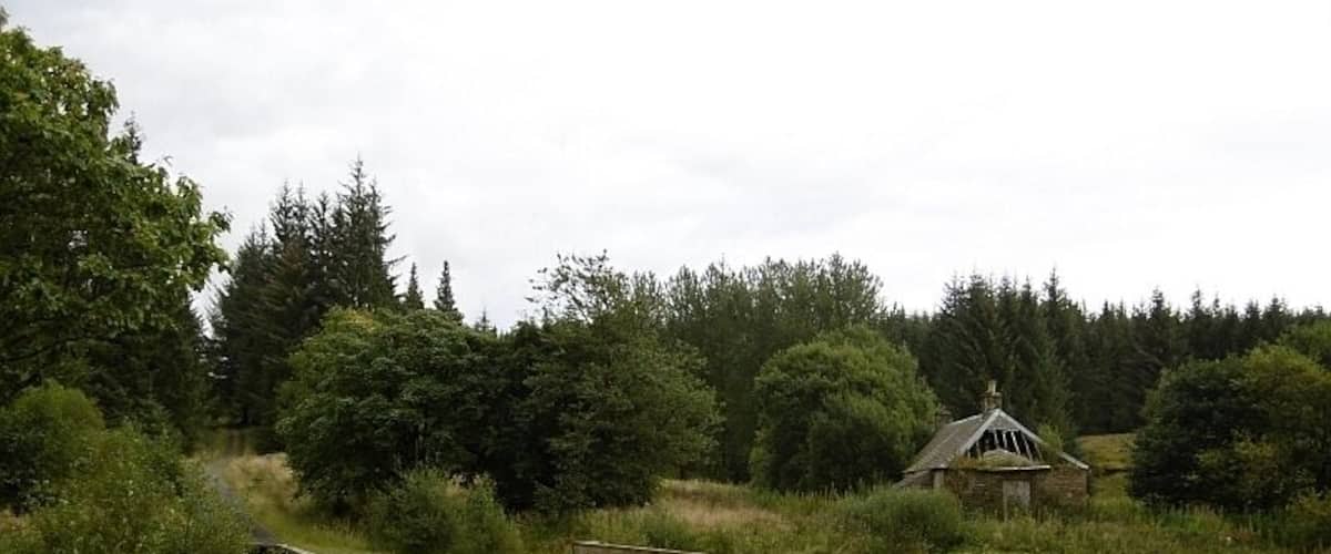 A wooden bridge over a gravel path with a stone building in the background.