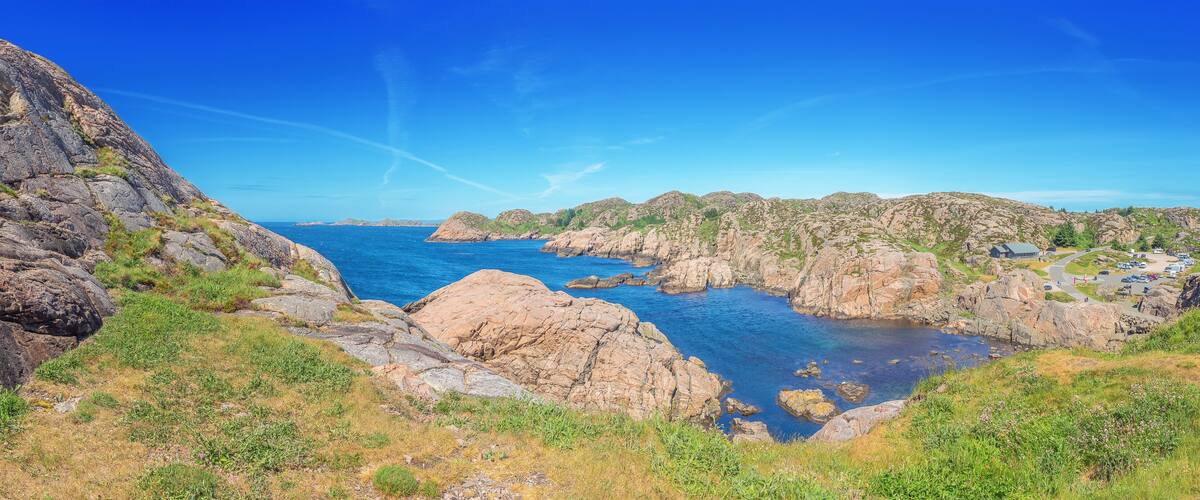 A coastal landscape with rocky cliffs, a clear blue sea, and a small settlement with buildings.