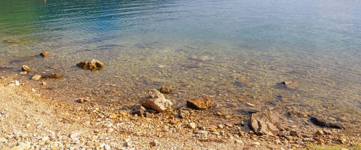 A clear lake with a rocky shoreline, a distant town, and mountains in the background.