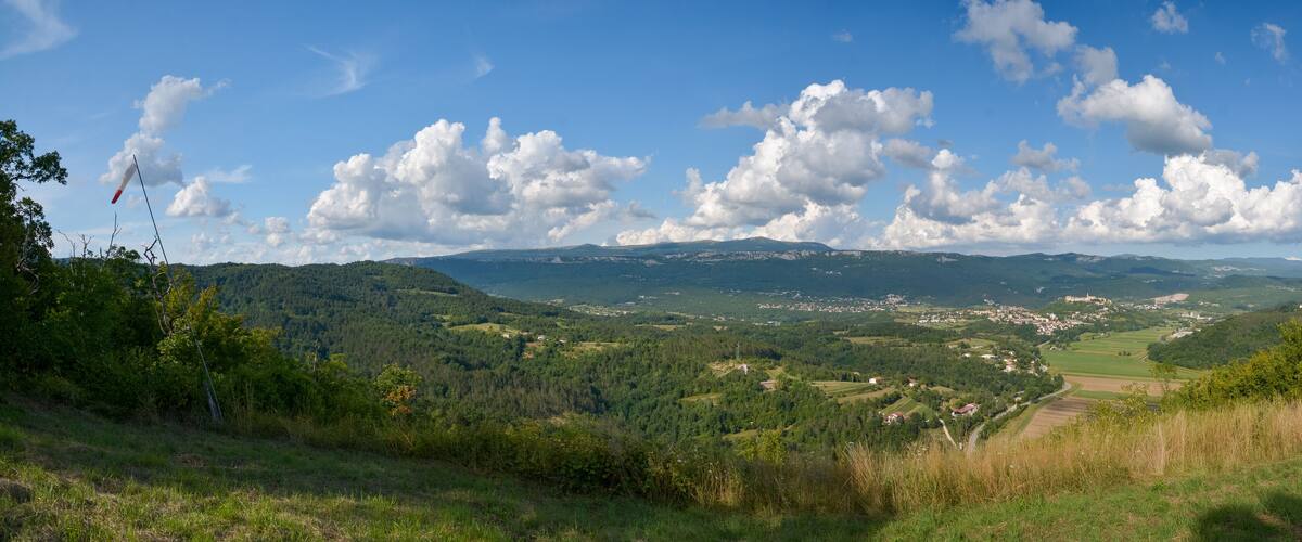 A valley with rolling hills, scattered houses, and a flag on a pole.