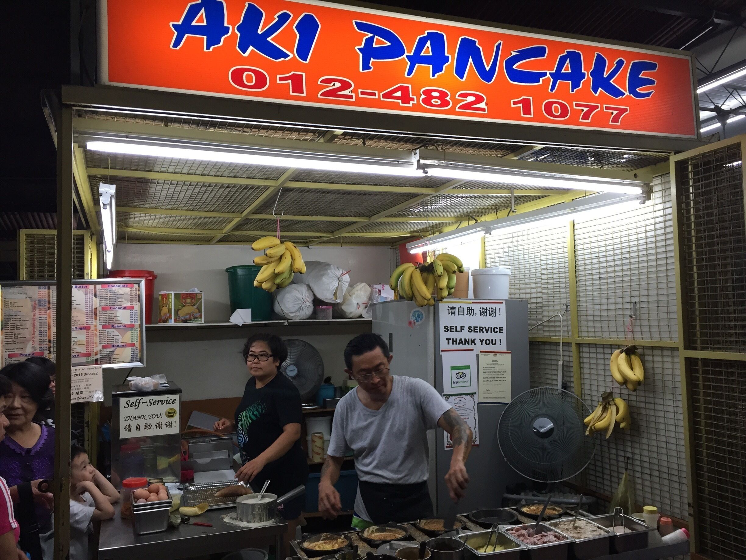 A street food stall named "Aki Pancake" with a phone number 012-482-1077.