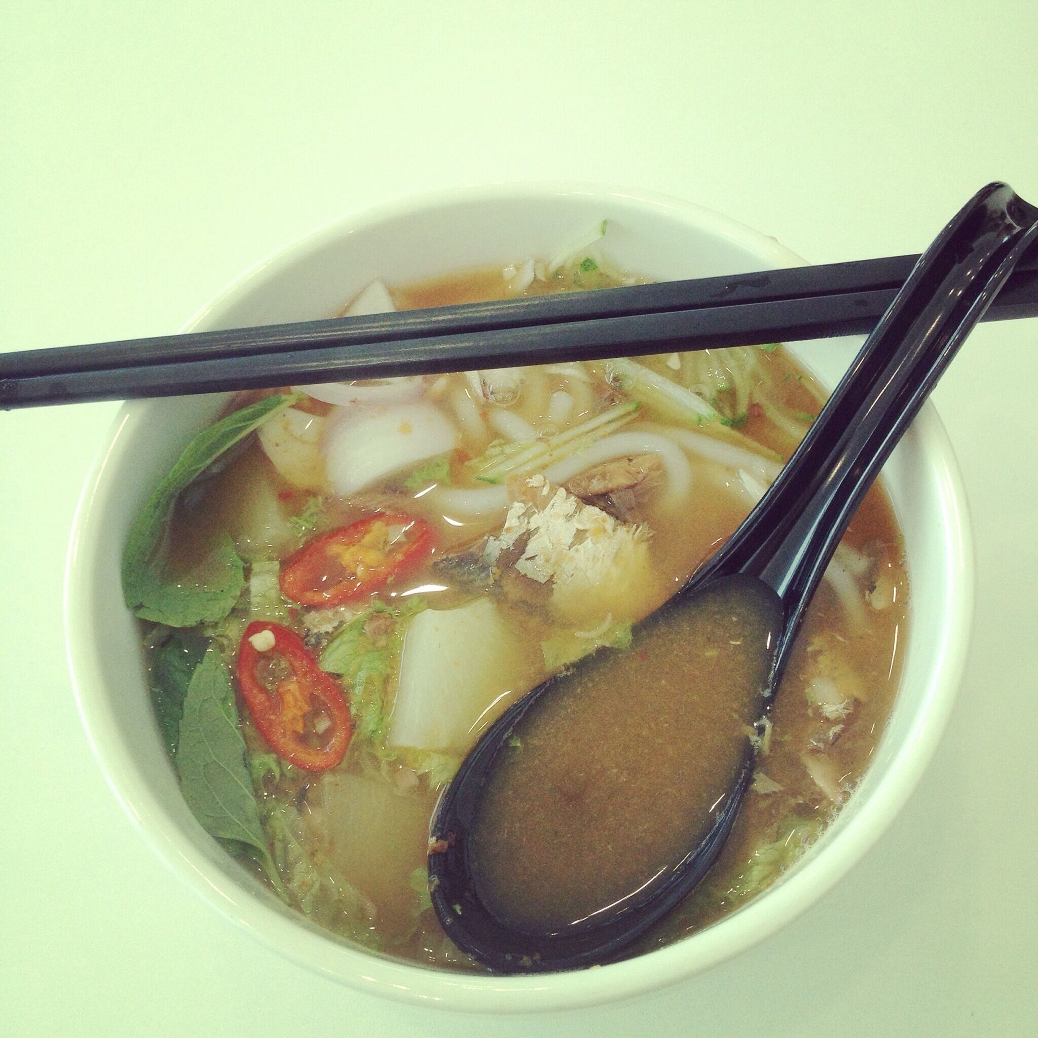 A bowl of soup with noodles, vegetables, and a spoon.