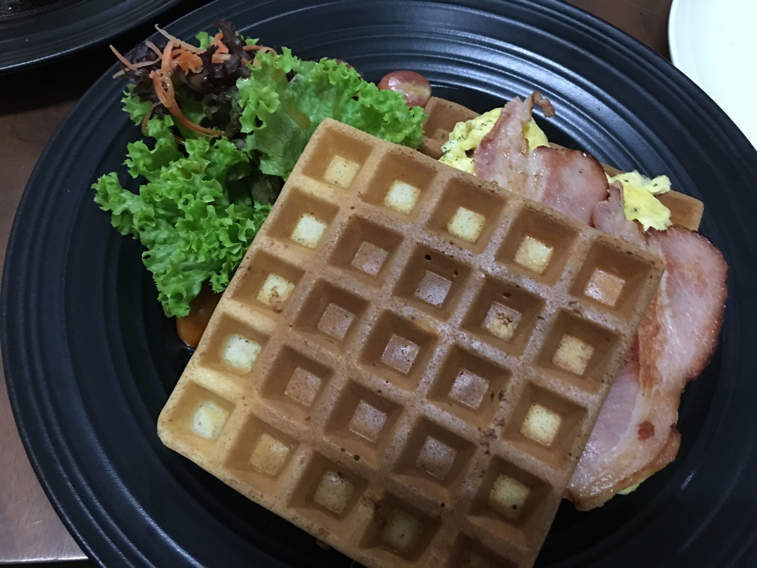 A waffle with bacon and greens on a plate.