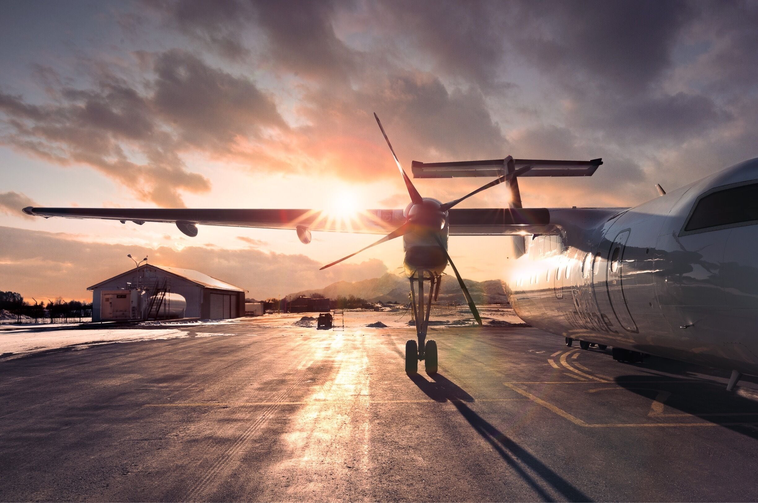 Un avión de hélice en una pista de aterrizaje con un atardecer de fondo.