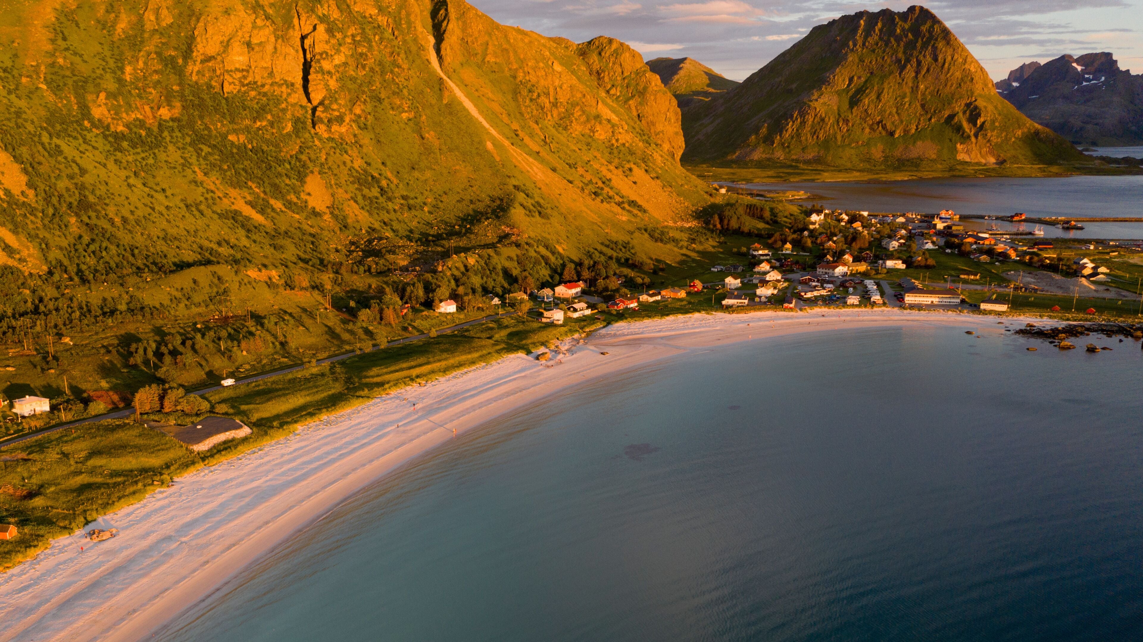 Un pueblo costero con playa, casas y montañas al fondo.