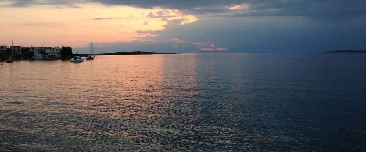 A coastal sunset with boats on calm waters and a distant landmass.